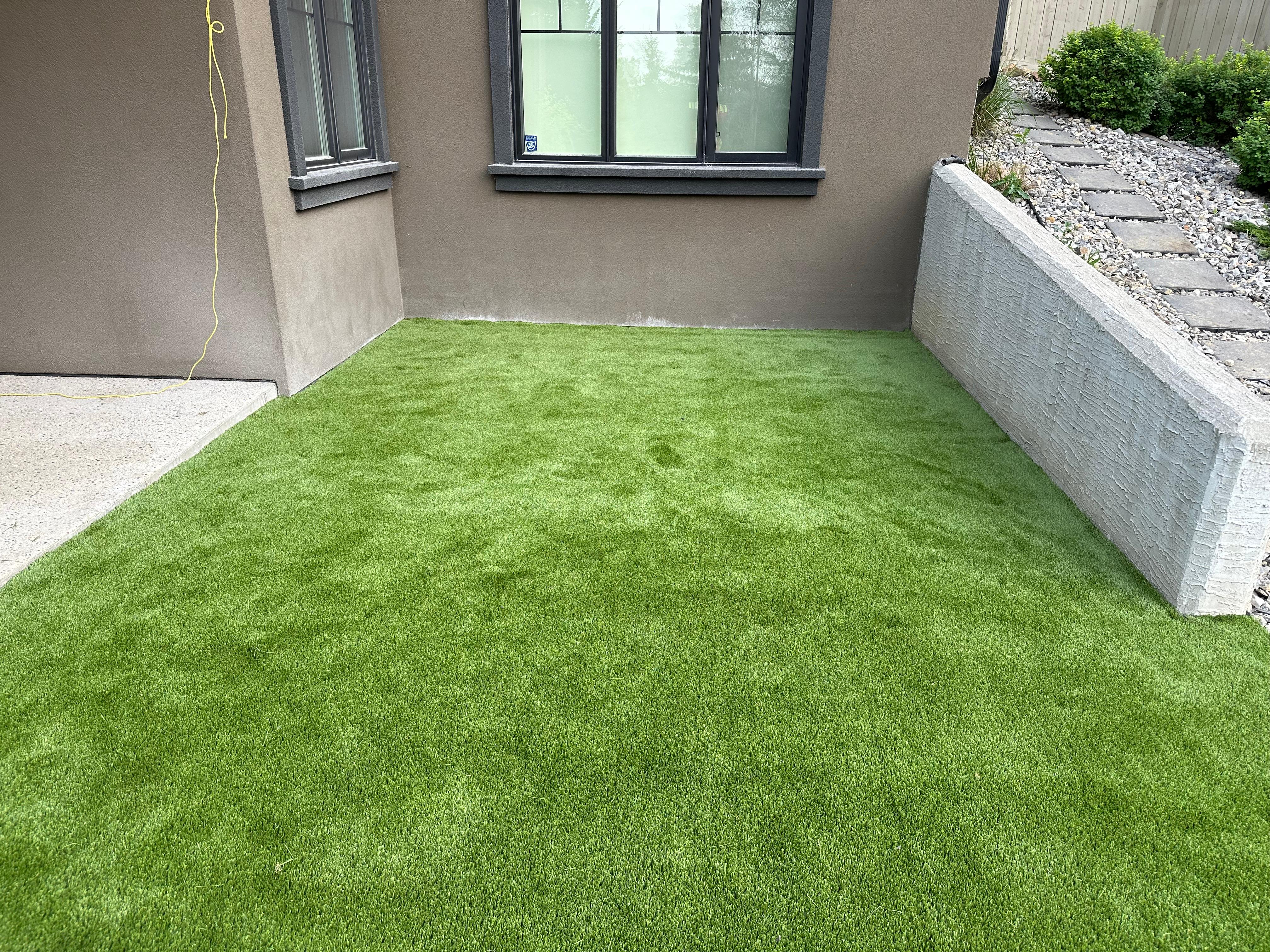 Artificial turf area beside house with grey stone retaining wall